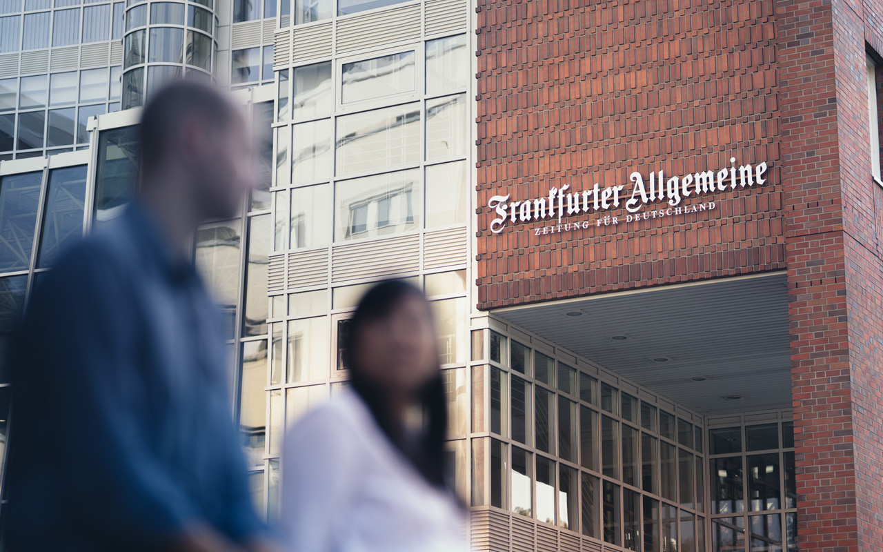 Zwei Personen (verschwommen) sitzend vor dem Redaktionsgebäude in Frankfurt